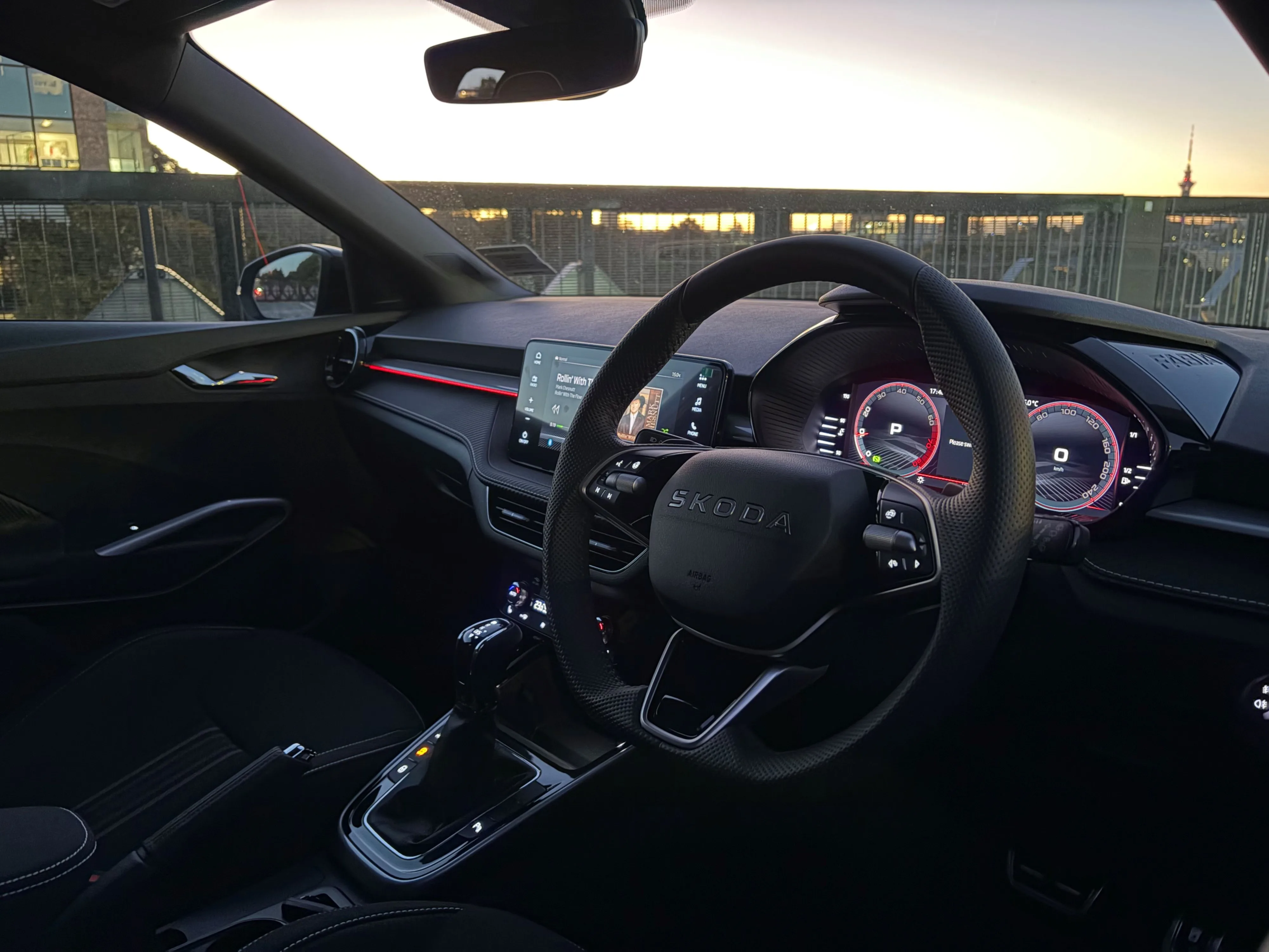 Interior/dashboard view of a 2026 Skoda Fabia 130 with the Auckland sunset through the windscreen.