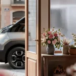 Teaser image of the new Kia PV7 in silver, front three quarters view as seen through an open door.
