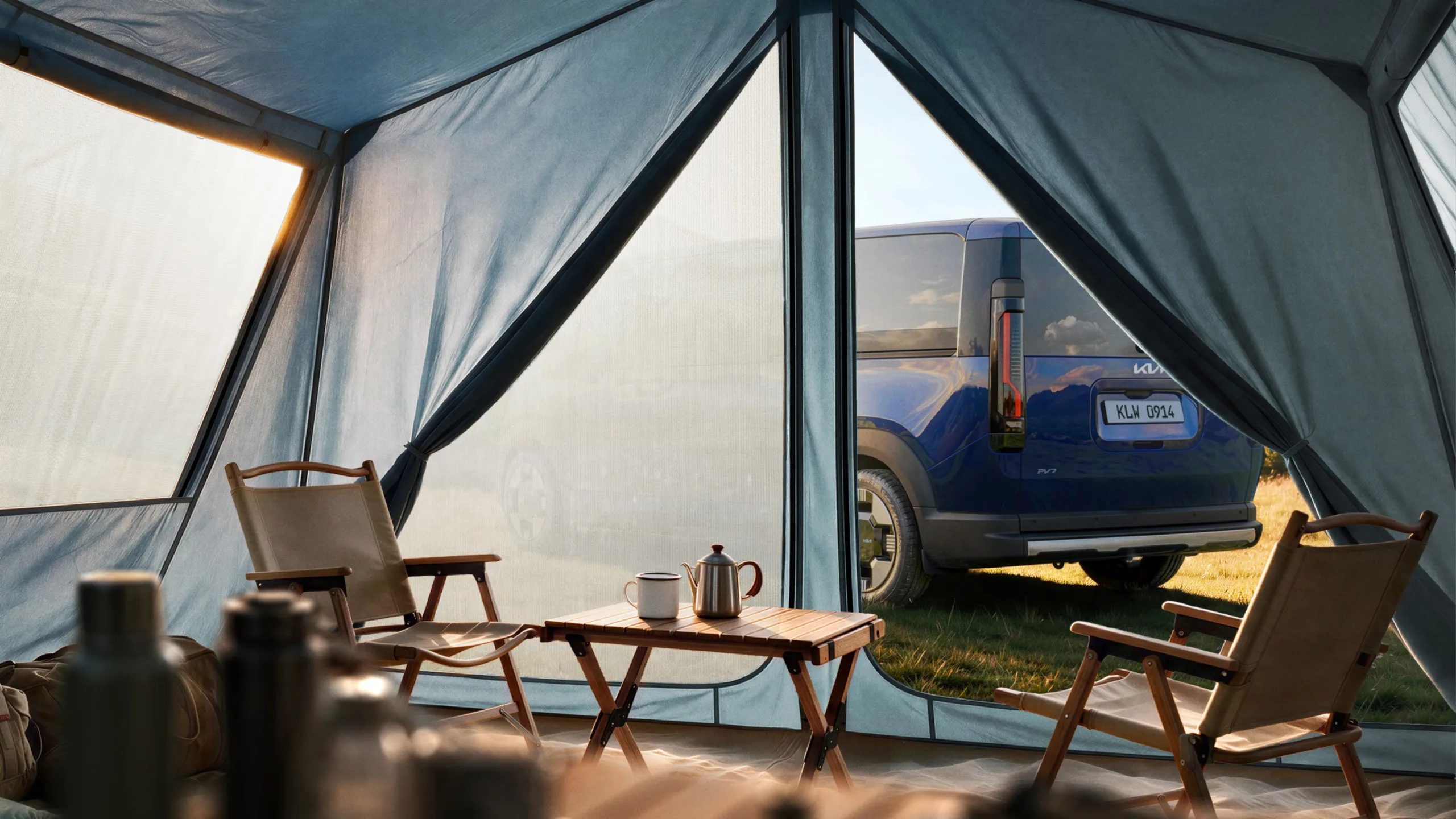 Teaser image of the new Kia PV7 in blue, rear three quarters view as seen through an open tent.