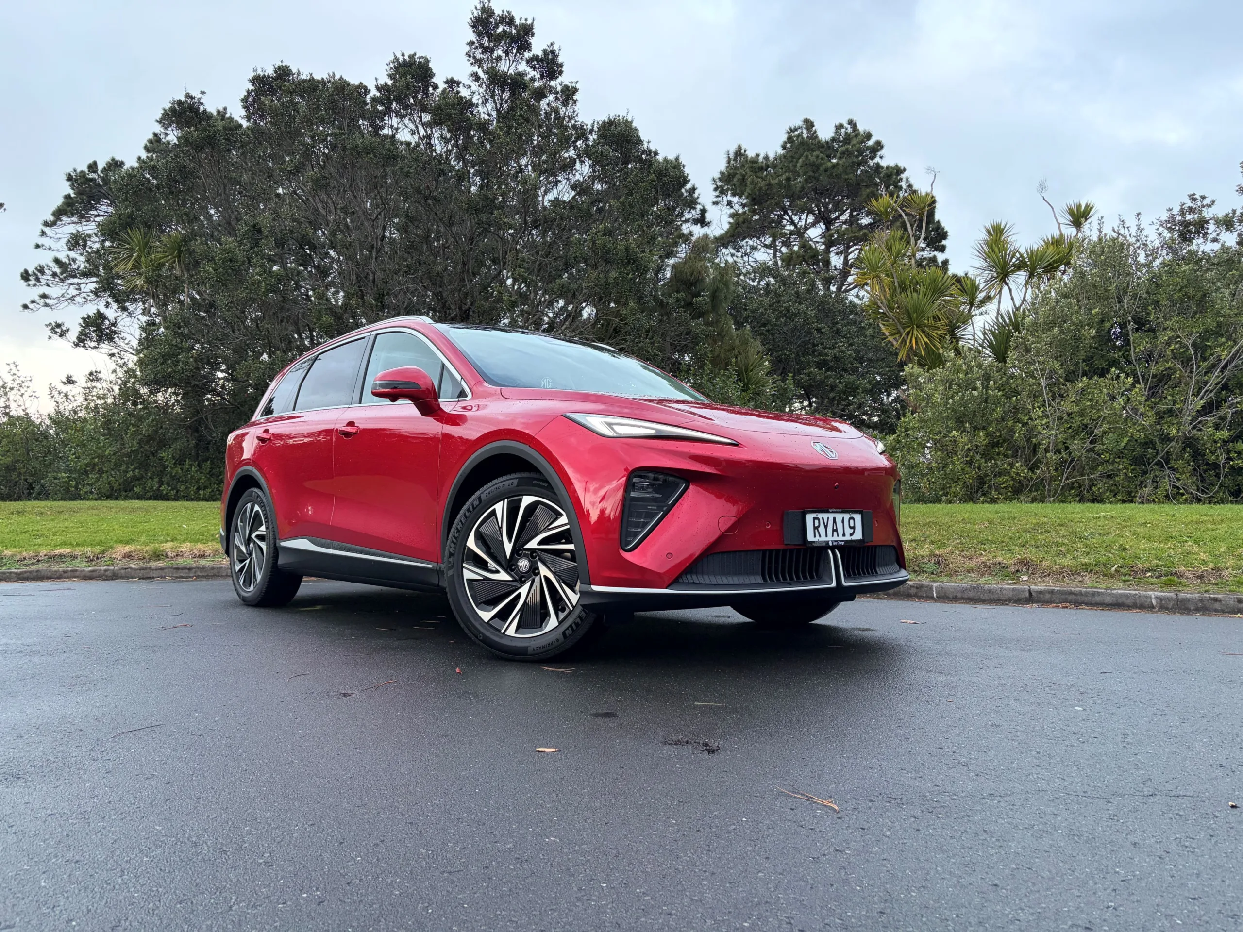 Front three quarters view of a 2026 MG S6 EV AWD in Diamond Red, nature/greenery in the background.