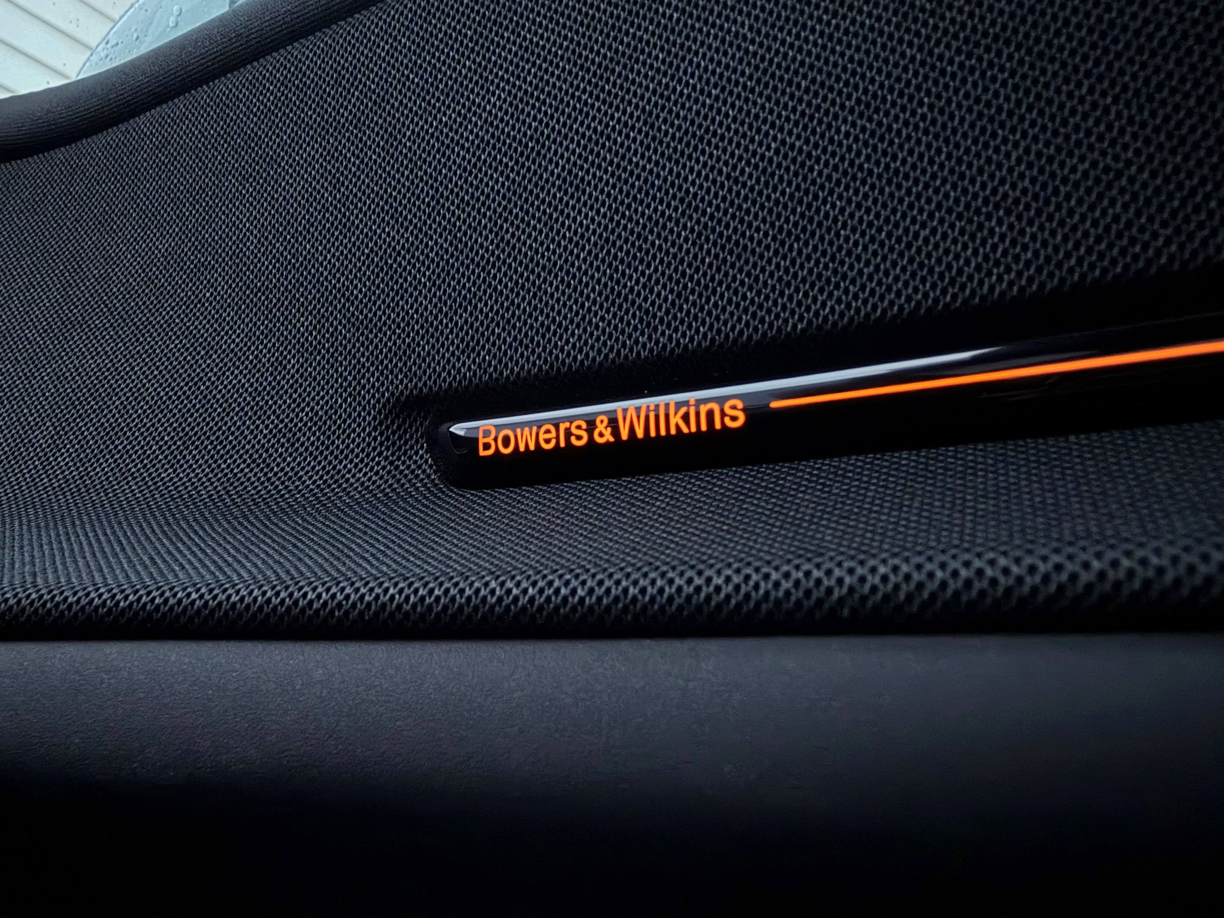 Photo of the Bowers & Wilkins logo, backlit in 'Swedish Gold' LED lighting on the driver side door of a 2026 Polestar 3 Performance.
