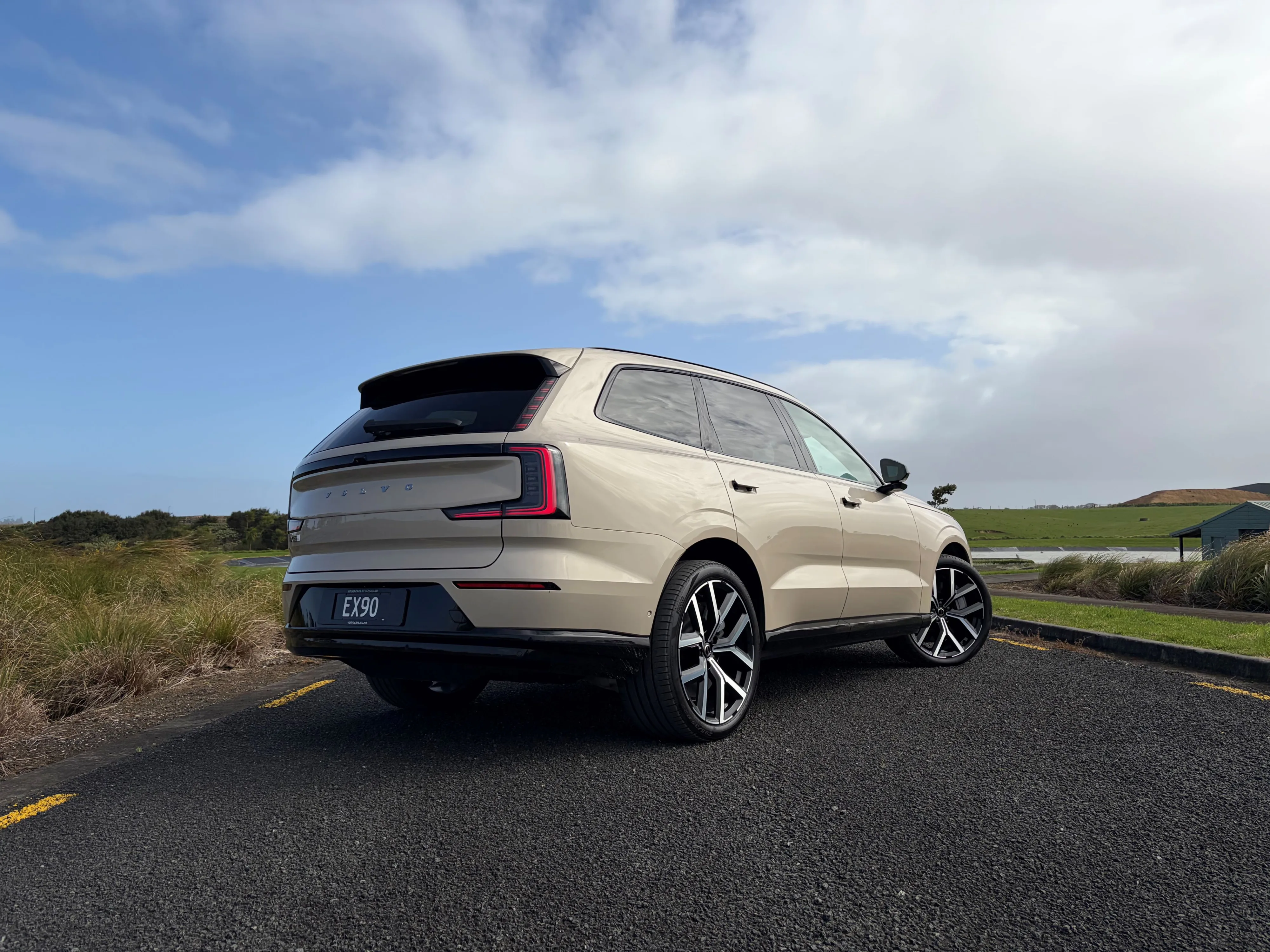 Rear three quarters view of a 2026 Volvo EX90 Ultra Twin Motor Performance in Sand Dune with a natural background.
